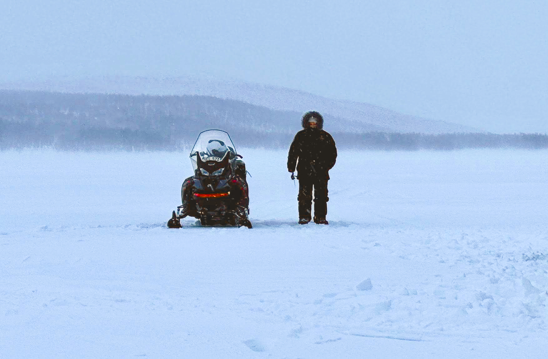 Guide and snowmobile on a frozen mountain lake